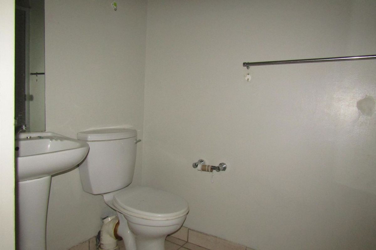 A compact bathroom featuring a pedestal sink, toilet, and tiled flooring, currently requiring cosmetic updates and repairs to wall surfaces and fixtures.