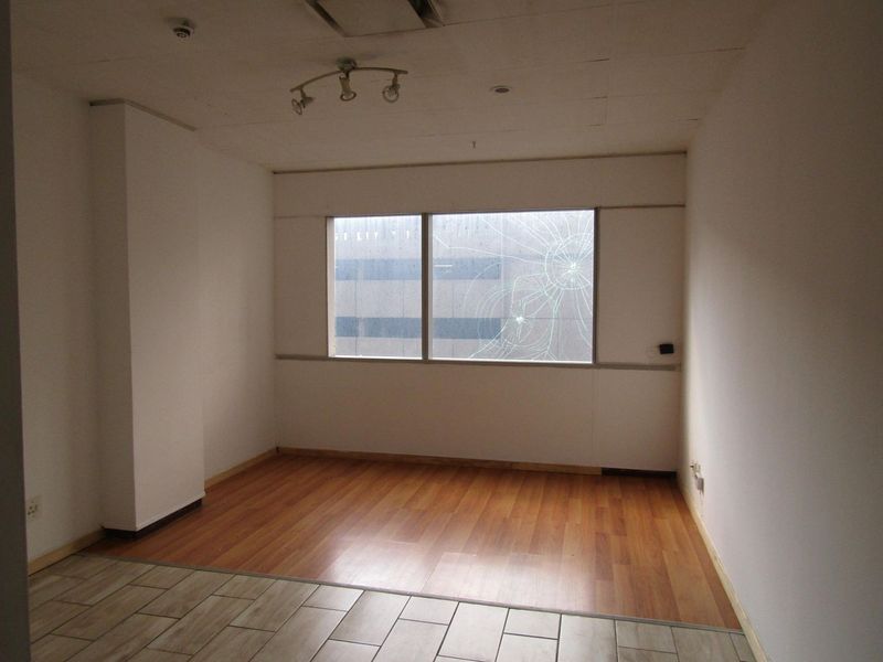 An empty bedroom featuring a mix of laminate and tiled flooring, track lighting, and a large window with a significant crack in the glass.