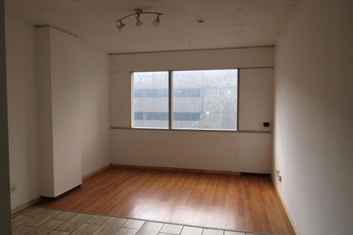 An empty bedroom featuring a mix of laminate and tiled flooring, track lighting, and a large window with a significant crack in the glass.