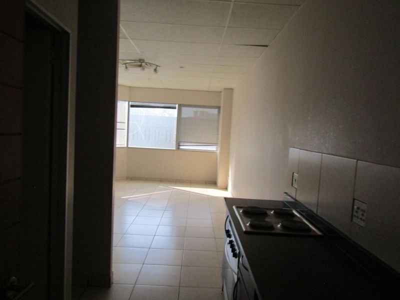 An open-plan living and kitchen area featuring tiled floors, a built-in electric hob, and large windows, currently vacant and in need of cosmetic updates.