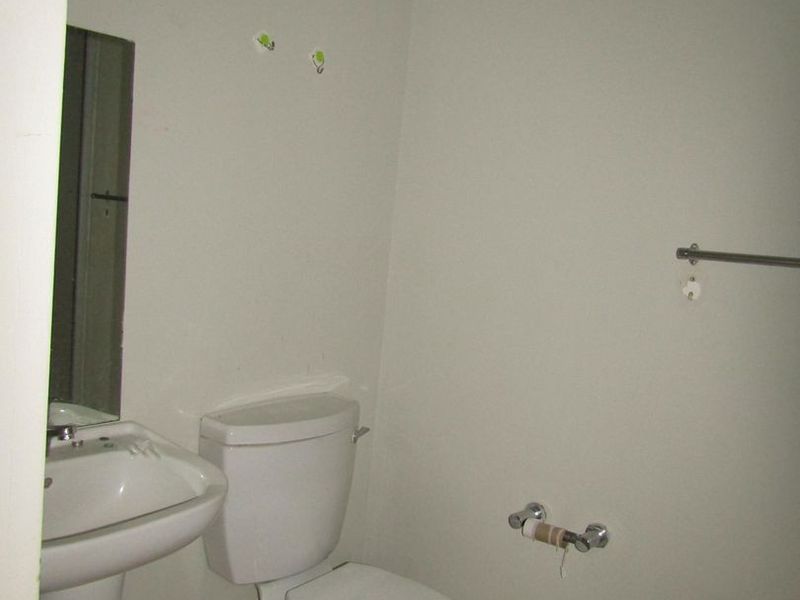 A compact bathroom featuring a pedestal basin, toilet, and tiled flooring, requiring minor cosmetic updates and repairs to fixtures.