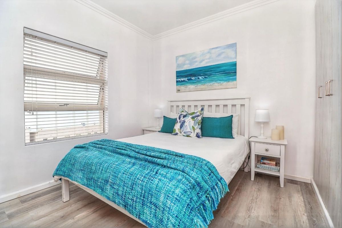 A bright and well-maintained bedroom featuring laminate flooring, a built-in wardrobe, and venetian blinds.