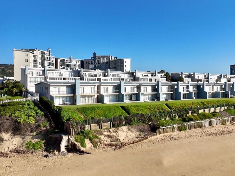 Aerial view of a beachfront apartment complex featuring landscaped lawns, private balconies, and direct access to the sandy coastline.