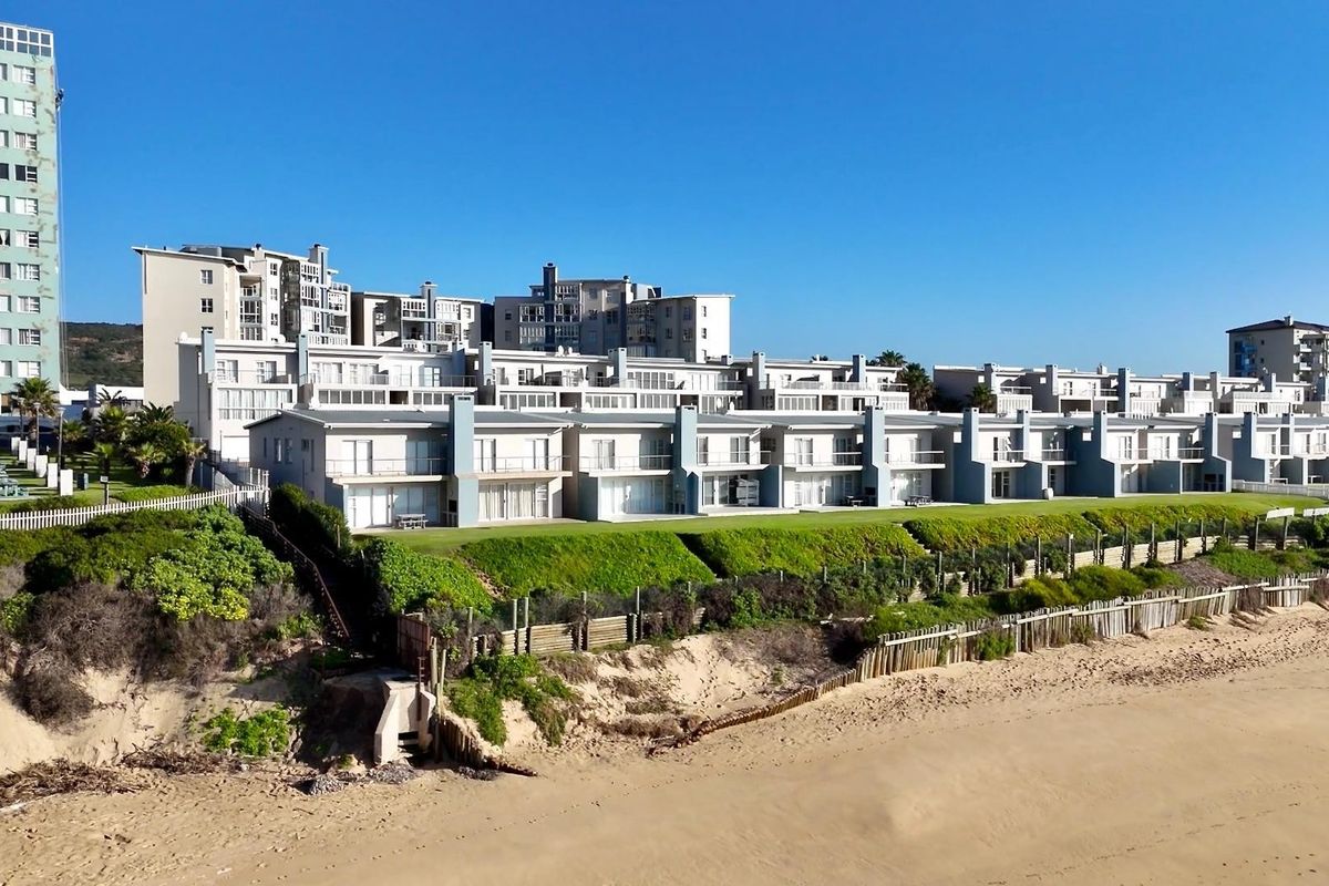 Aerial view of a beachfront apartment complex featuring landscaped lawns, private balconies, and direct access to the sandy coastline.