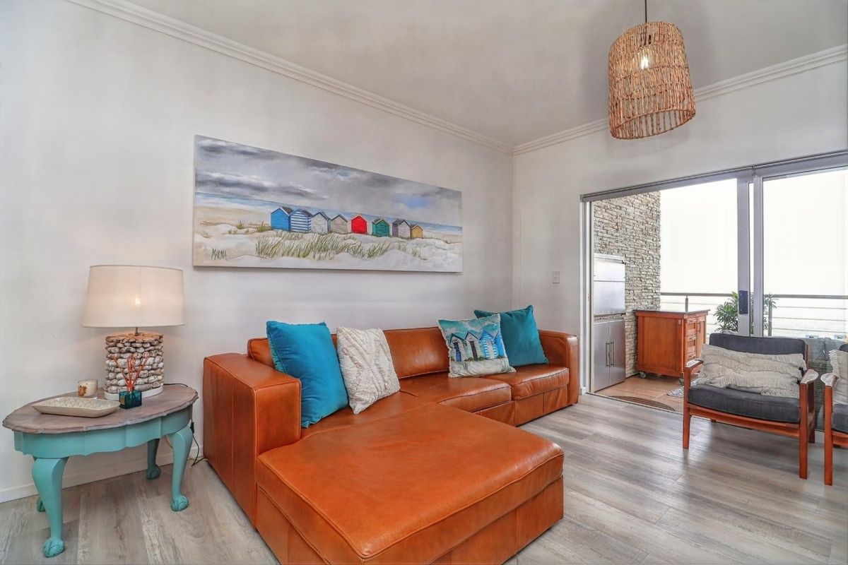 A bright living room featuring modern laminate flooring, cove cornicing, and a large sliding glass door providing access to an outdoor balcony area.