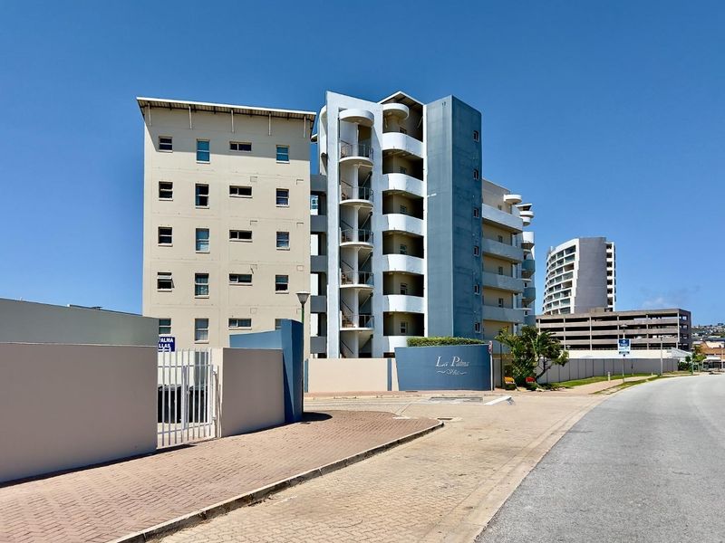 Exterior view of La Palma apartment complex featuring a multi-story building with balconies, security gate, and paved driveway access.