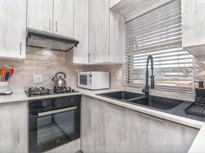 Modern kitchen featuring light wood-grain cabinetry, subway tile backsplash, integrated gas hob, electric oven, and a sleek double basin sink with a gooseneck faucet.