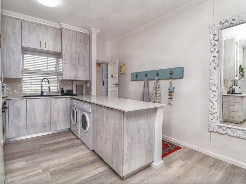 A functional kitchen featuring light wood-look cabinetry, stone countertops, integrated laundry appliances, and a clean, modern aesthetic.