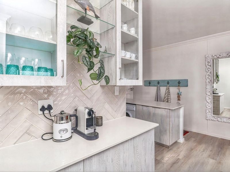 A well-maintained kitchen area featuring light wood-grain cabinetry, stone countertops, and a stylish herringbone tile backsplash with integrated laundry space.