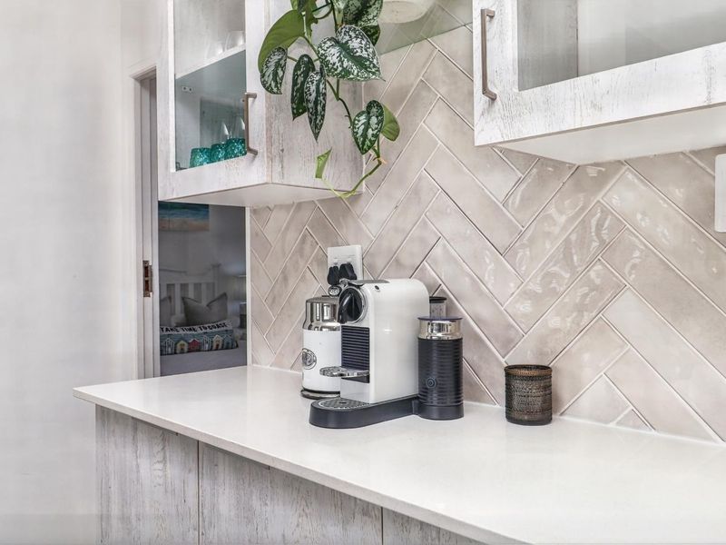 A modern kitchen area featuring a stylish herringbone tile backsplash, white quartz countertops, and light-toned cabinetry.