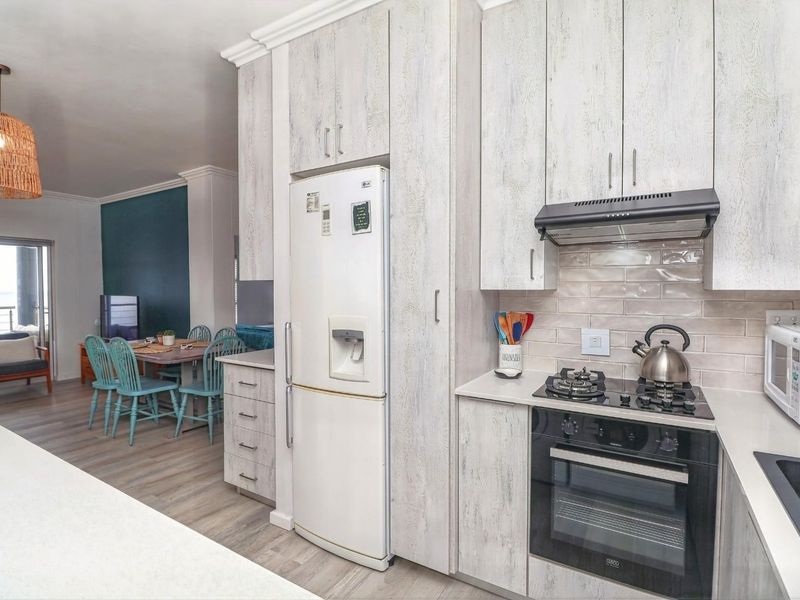 Modern open-plan kitchen featuring light wood-grain cabinetry, stone countertops, and integrated appliances, flowing seamlessly into the adjacent dining and living area.