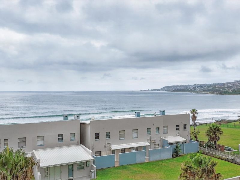 Elevated view overlooking the ocean, coastline, and well-maintained communal garden areas of the apartment complex.