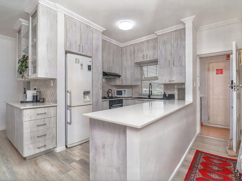Modern kitchen featuring light wood-grain cabinetry, quartz countertops, a breakfast bar, and integrated appliances, finished with crown molding and contemporary fixtures.