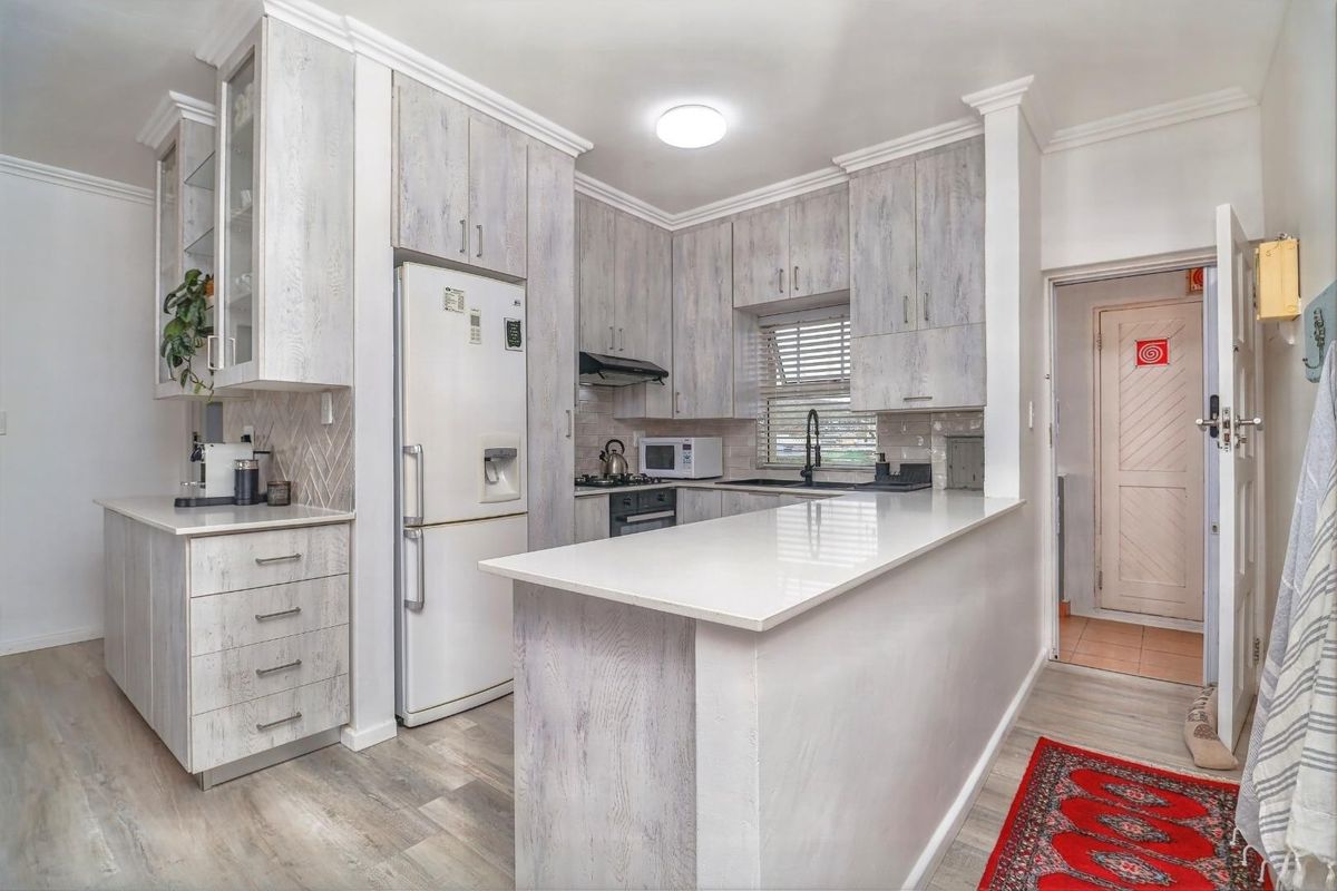 Modern kitchen featuring light wood-grain cabinetry, quartz countertops, a breakfast bar, and integrated appliances, finished with crown molding and contemporary fixtures.