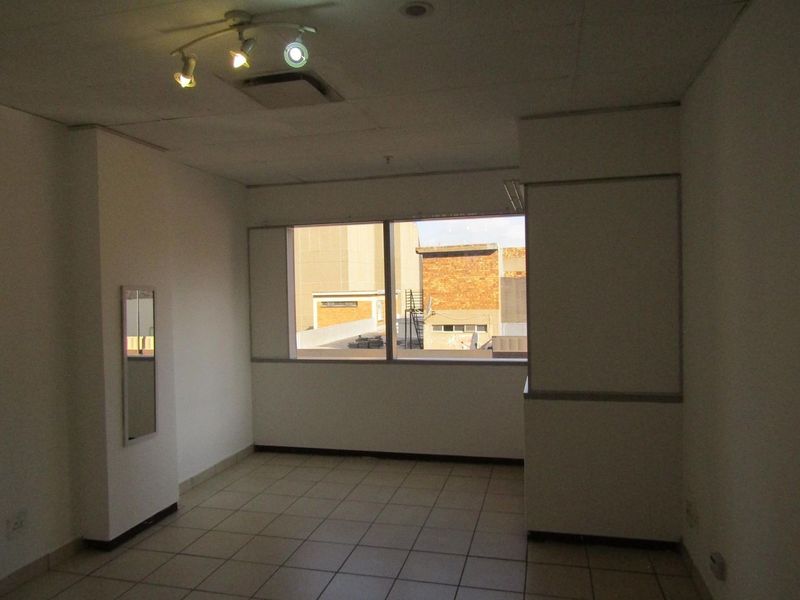 An empty bedroom featuring tiled flooring, a large window with urban views, and a ceiling-mounted spotlight fixture.