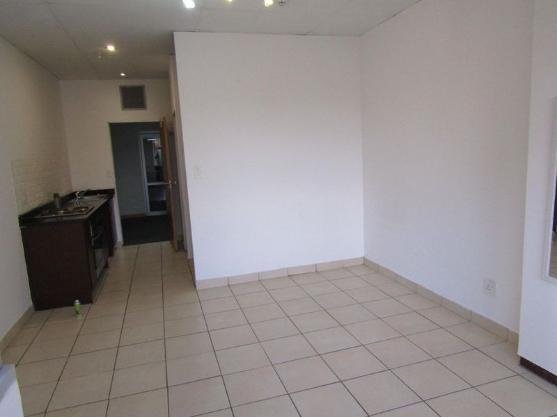 An empty open-plan living and kitchen area featuring tiled flooring, built-in cabinetry, and a functional kitchenette.