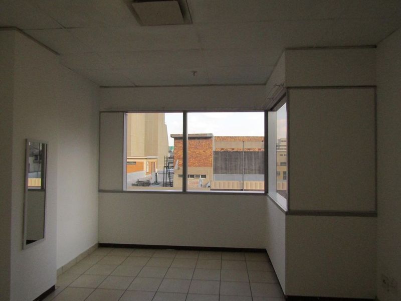 An empty bedroom featuring tiled flooring, a corner window with urban views, and a drop ceiling. The space requires cosmetic updates.