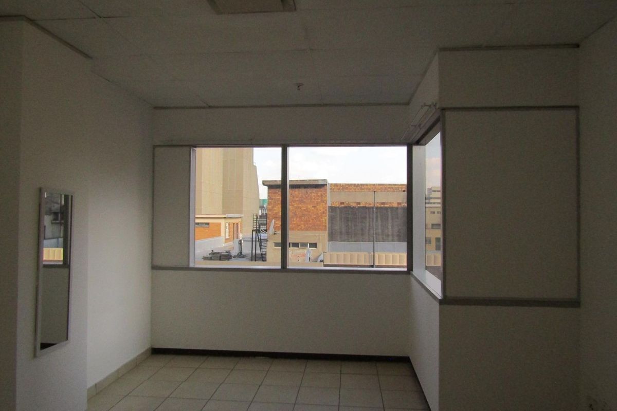 An empty bedroom featuring tiled flooring, a corner window with urban views, and a drop ceiling. The space requires cosmetic updates.