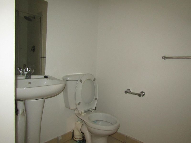 A basic bathroom featuring a pedestal basin, toilet, and wall-mounted mirror, requiring minor cosmetic updates to the exposed plumbing and finishes.