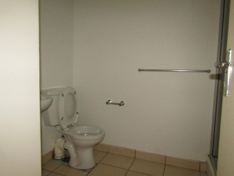 A basic, empty bathroom featuring a toilet, tiled flooring, and a shower enclosure. The space requires cosmetic updates and minor plumbing repairs.