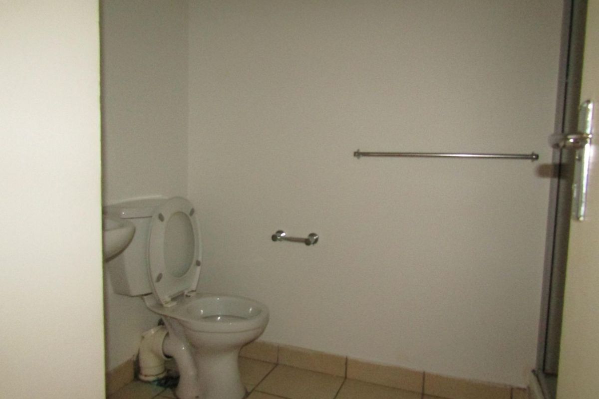 A basic, empty bathroom featuring a toilet, tiled flooring, and a shower enclosure. The space requires cosmetic updates and minor plumbing repairs.