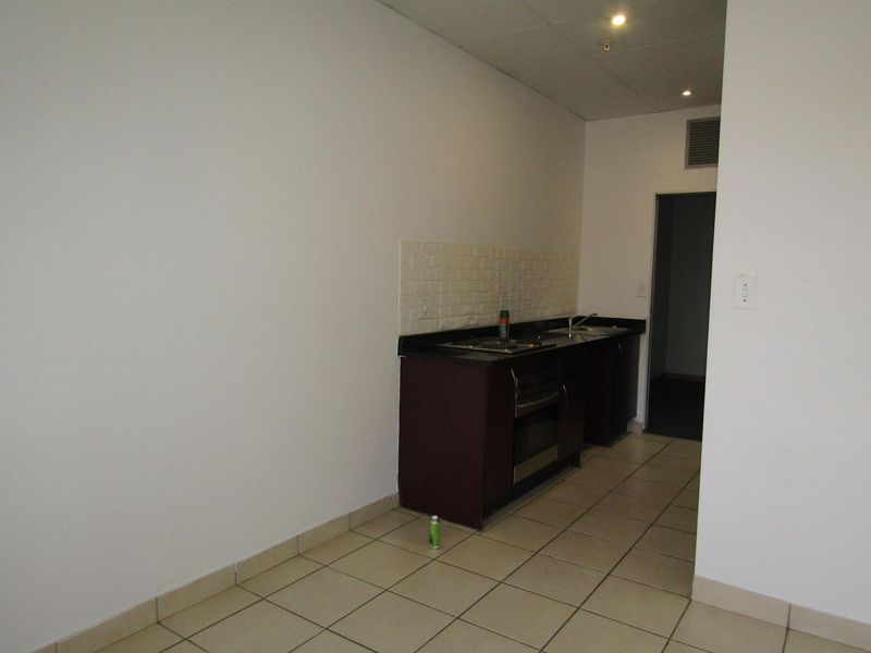 A compact, empty kitchen area featuring dark cabinetry, a built-in oven and hob, tiled flooring, and a tiled backsplash.