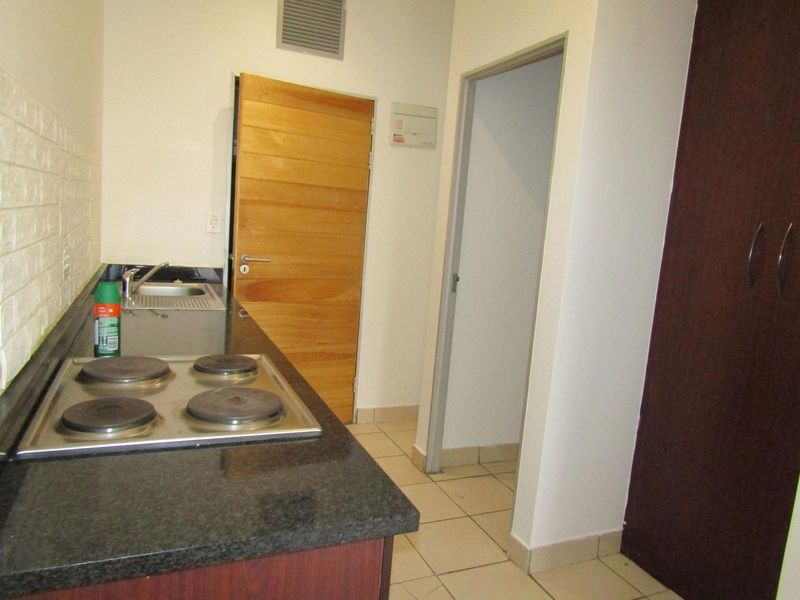 Compact kitchen featuring granite countertops, an electric hob, stainless steel sink, and built-in cabinetry with tiled flooring.