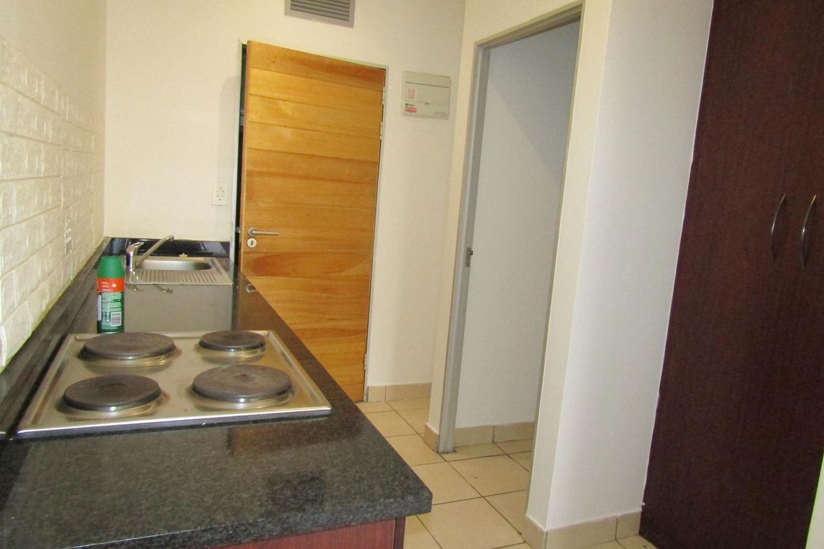 Compact kitchen featuring granite countertops, an electric hob, stainless steel sink, and built-in cabinetry with tiled flooring.