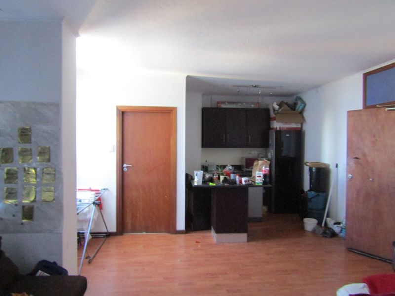 Open plan living area featuring laminate flooring and a compact kitchen with dark cabinetry and a central island.