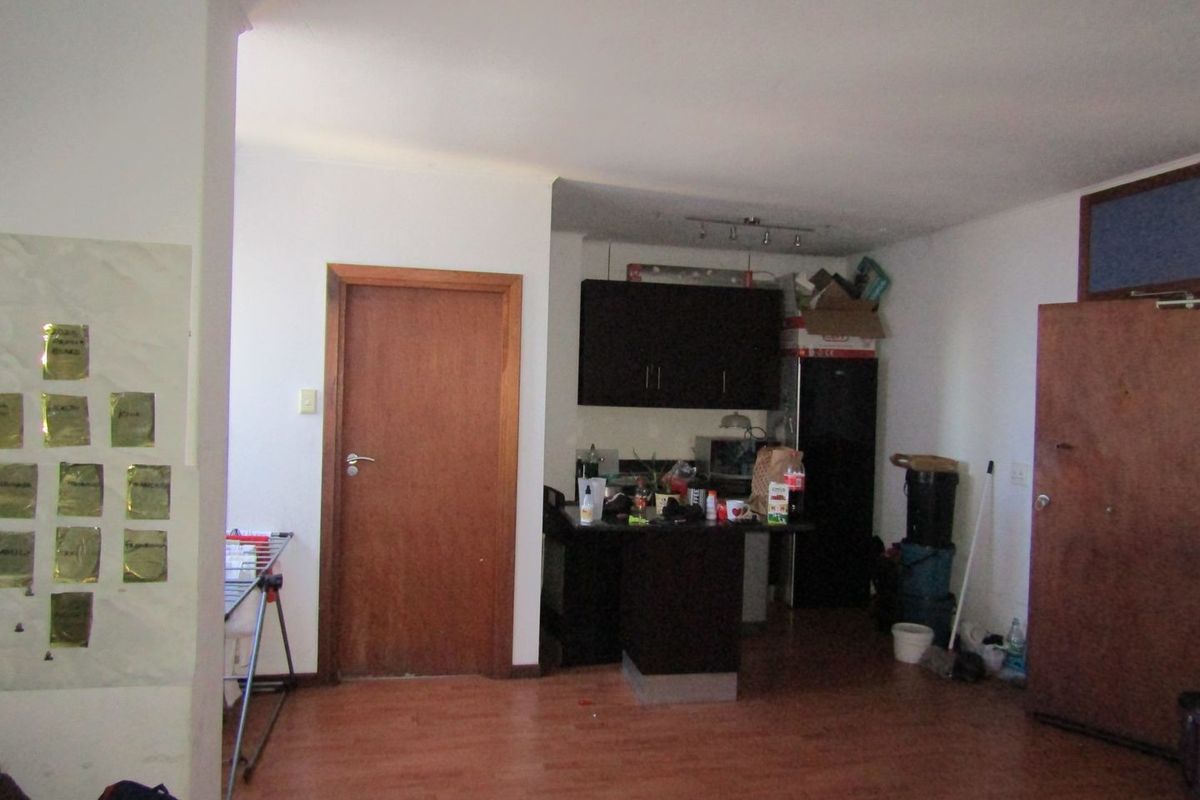 Open plan living area featuring laminate flooring and a compact kitchen corner with dark cabinetry.