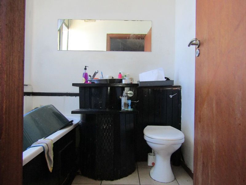 A dated bathroom featuring a bathtub, toilet, and vanity unit with a wall-mounted mirror, requiring cosmetic updates to modernize the space.