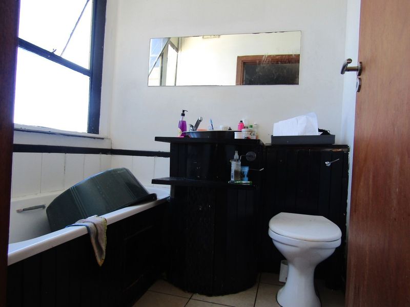 A dated bathroom featuring a bathtub, toilet, and vanity unit with a wall-mounted mirror, requiring cosmetic updates to improve its overall condition.