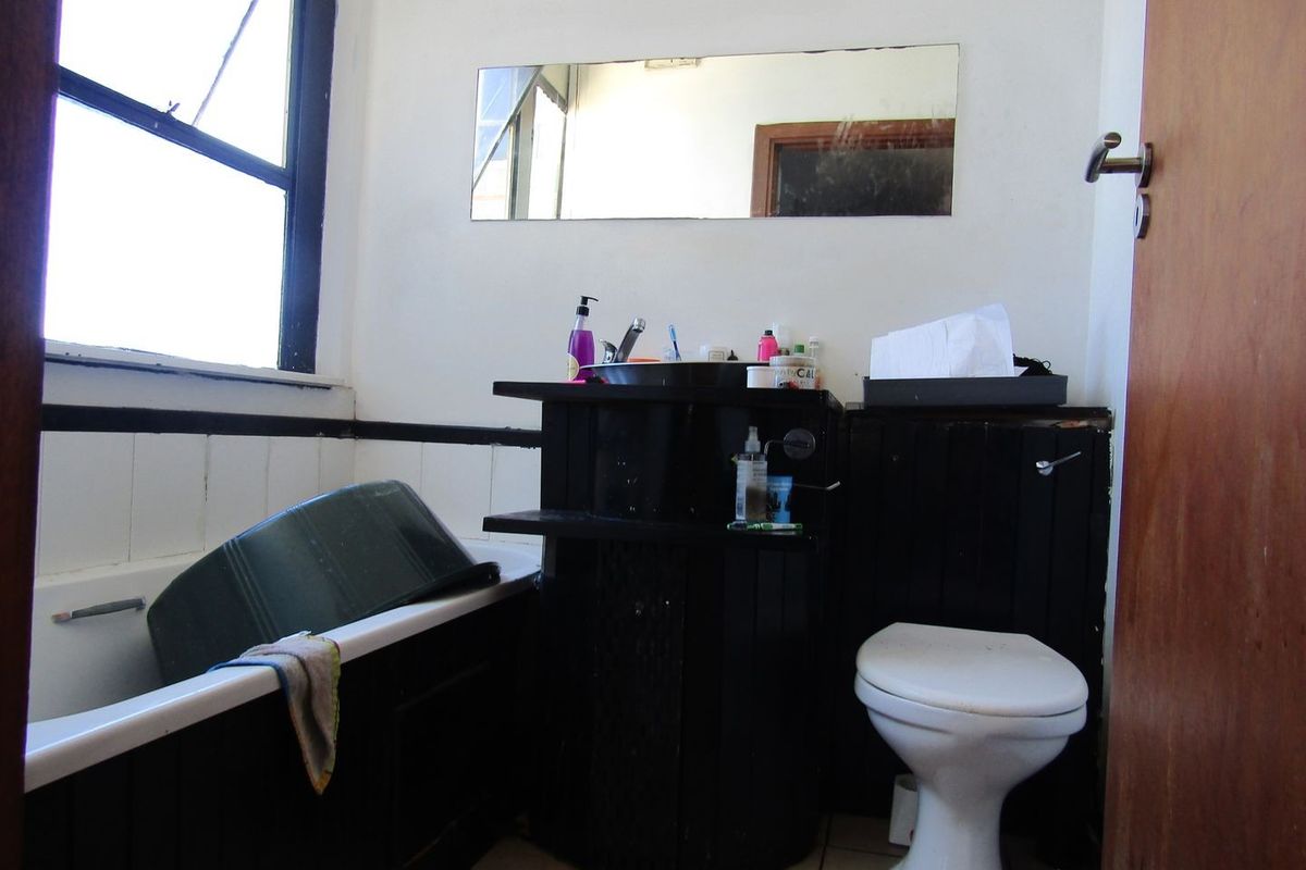A dated bathroom featuring a bathtub, toilet, and vanity unit with a wall-mounted mirror, requiring cosmetic updates to improve its overall condition.