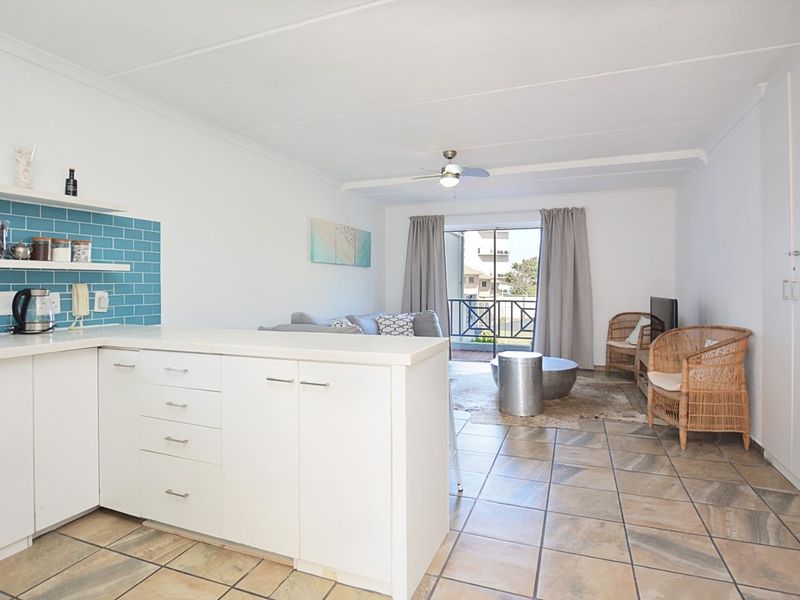 Open-plan living area featuring a kitchen with blue subway tile backsplash, tiled flooring, and a sliding door leading to a balcony.