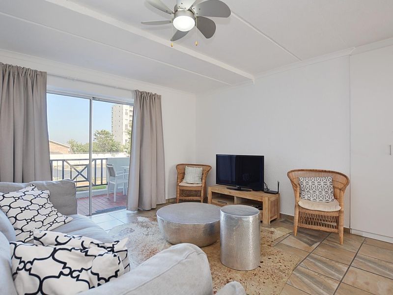 A bright living room featuring tiled flooring, a ceiling fan, and a sliding glass door providing access to a balcony.