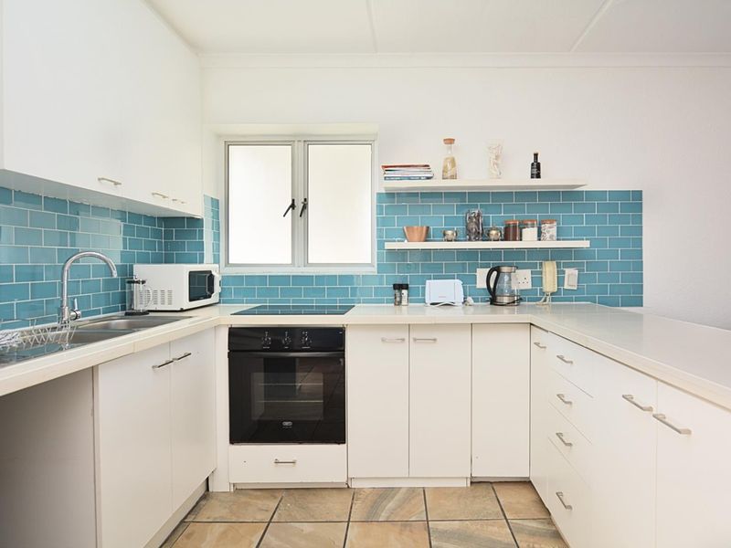 A functional kitchen featuring white cabinetry, a blue subway tile backsplash, built-in oven, electric hob, and tiled flooring.