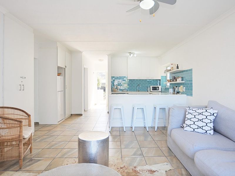 Bright open-plan living area featuring tiled floors, a functional kitchen with a blue subway tile backsplash, and a central island with breakfast bar seating.