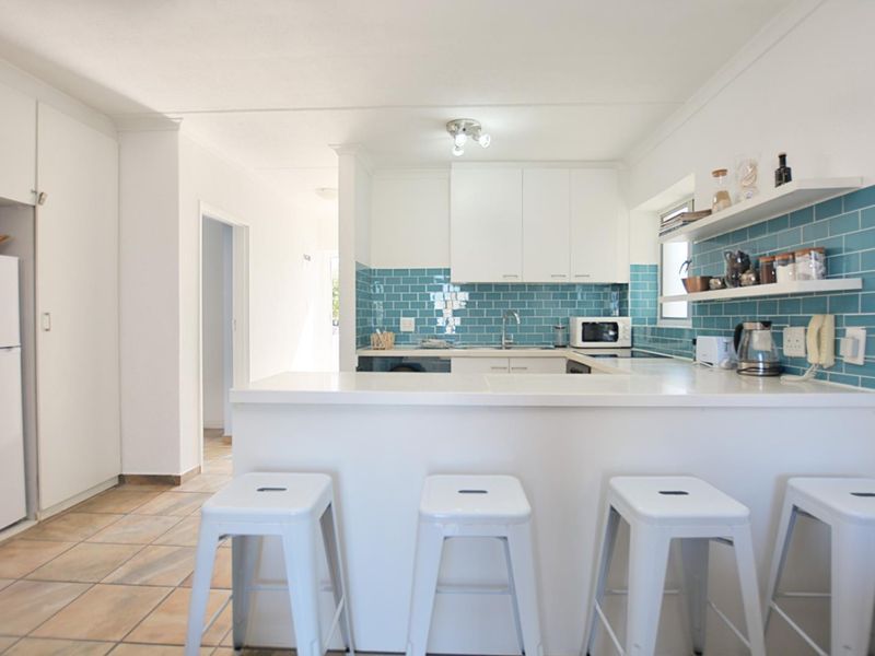 A bright, functional kitchen featuring white cabinetry, a striking blue subway tile backsplash, a breakfast bar, and open shelving for storage.