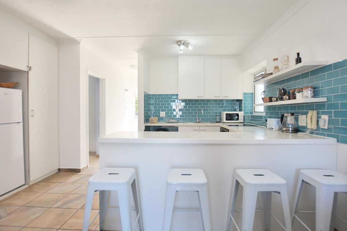 A bright, functional kitchen featuring white cabinetry, a striking blue subway tile backsplash, a breakfast bar, and open shelving for storage.