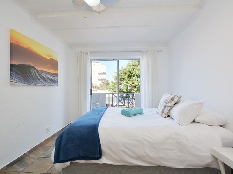 A bright bedroom featuring tiled flooring, a ceiling fan, and a sliding glass door providing access to an outdoor balcony.