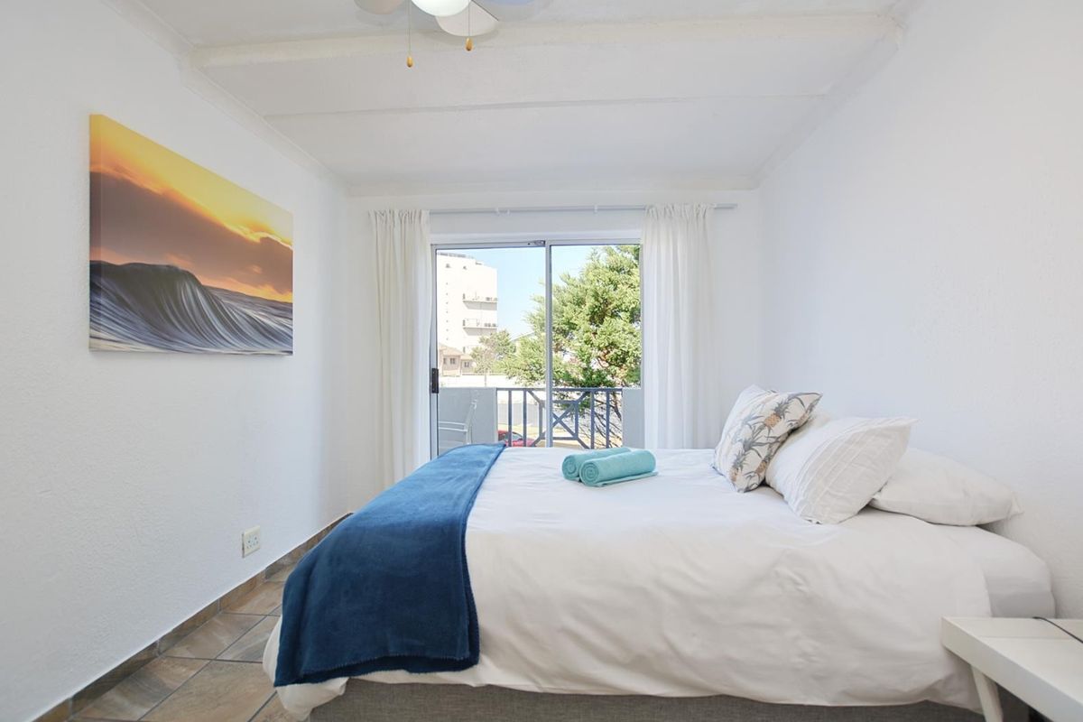 A bright bedroom featuring tiled flooring, a ceiling fan, and a sliding glass door providing access to an outdoor balcony.