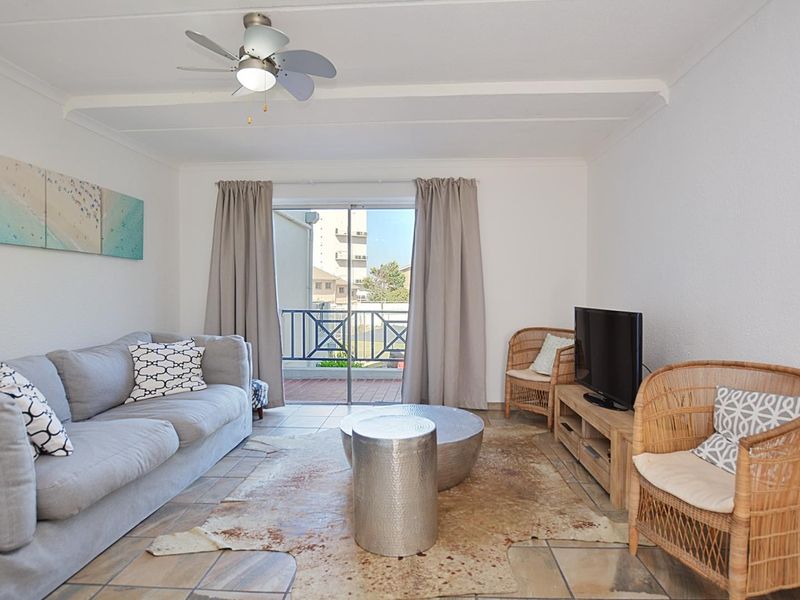 A bright living room featuring tiled flooring, a ceiling fan, and sliding glass doors that open onto a private balcony.