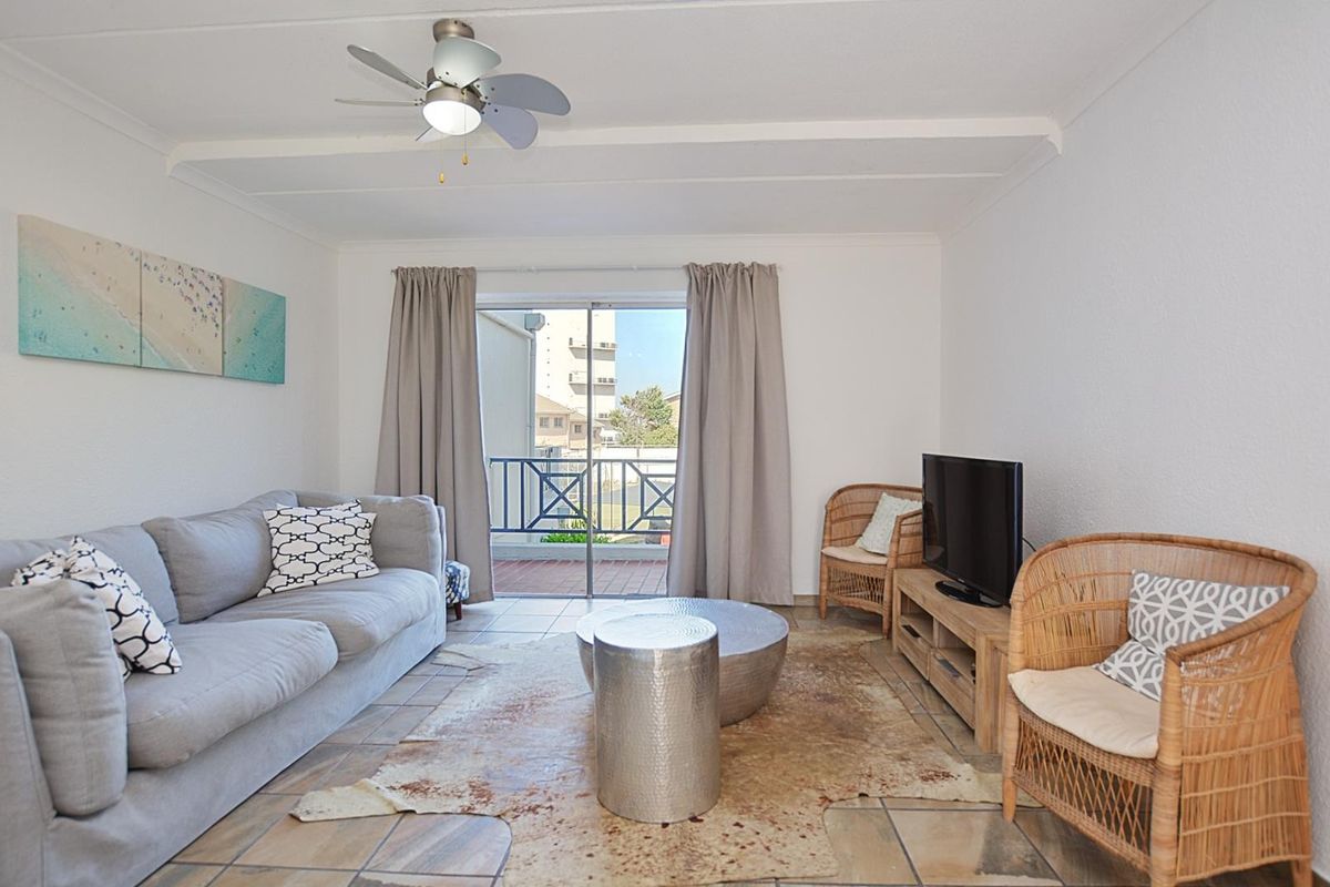 A bright living room featuring tiled flooring, a ceiling fan, and sliding glass doors that open onto a private balcony.