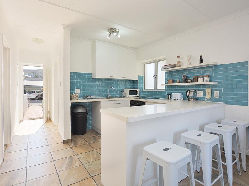 A bright, functional kitchen featuring white cabinetry, a blue subway tile backsplash, and a breakfast bar, with direct access to the hallway.