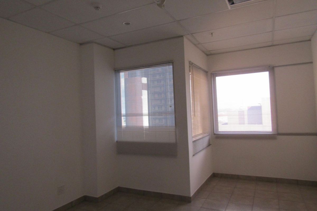 An empty room featuring tiled flooring, suspended ceiling tiles, and venetian blinds on the windows.
