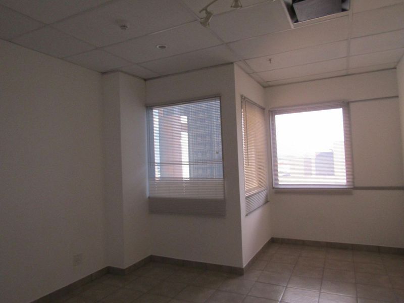An empty room featuring tiled flooring, suspended ceiling tiles, and venetian blinds on the windows.