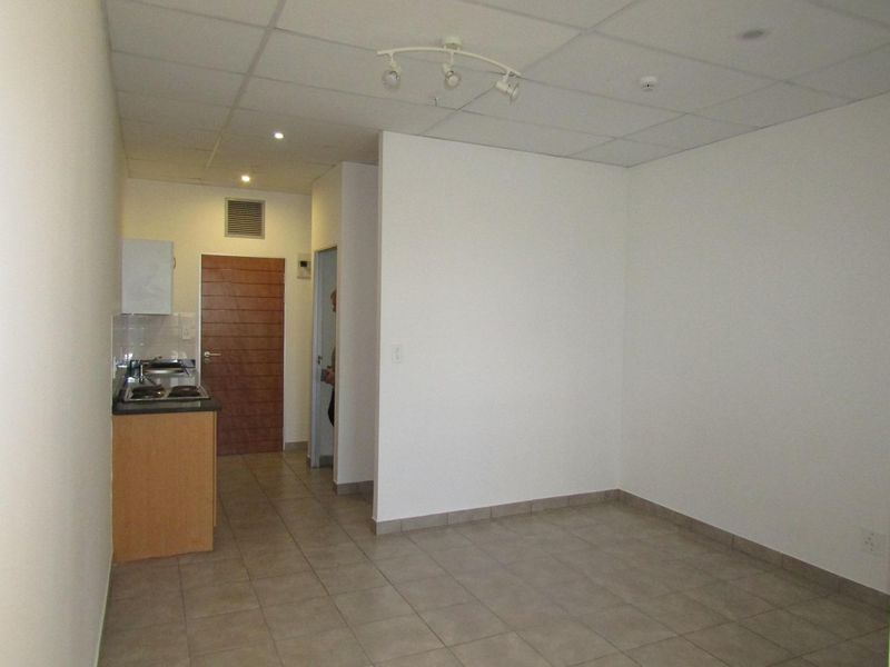 An open-plan living area featuring tiled flooring, a drop ceiling, and a compact kitchenette with built-in cabinetry and an electric hob.