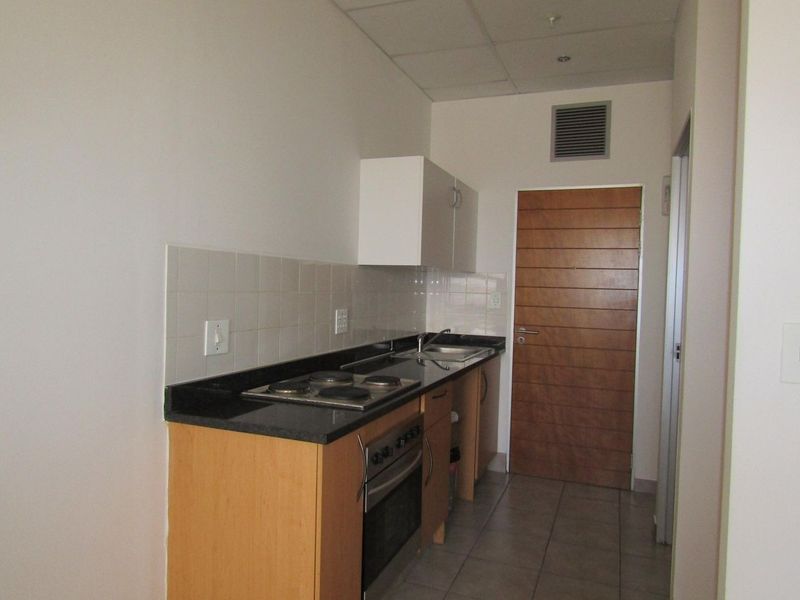 A compact, functional kitchen featuring built-in cabinetry, granite countertops, an electric hob, an oven, and a tiled backsplash.