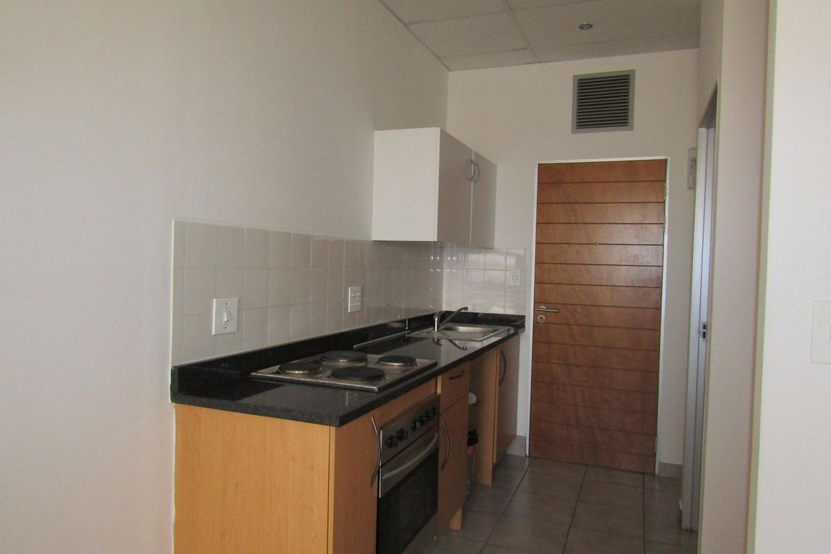 A compact, functional kitchen featuring built-in cabinetry, granite countertops, an electric hob, an oven, and a tiled backsplash.