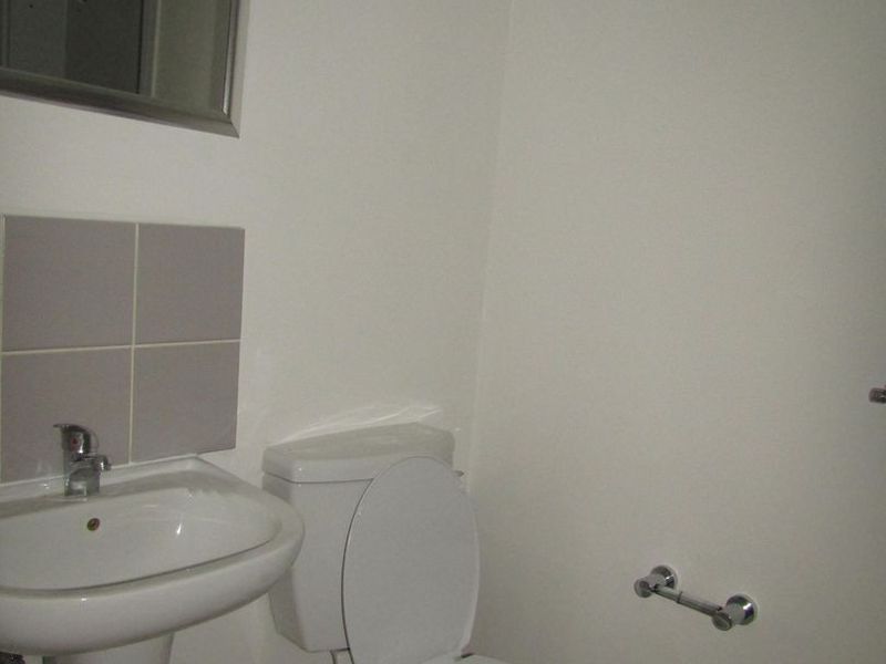 A functional bathroom featuring a pedestal basin, toilet, and wall-mounted mirror with neutral wall finishes and tiled splashback.